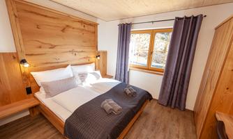 A cozy bedroom with wooden decor and a large window. There is a double bed and a pleasant atmosphere.