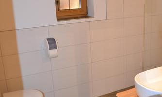 A modern bathroom with neutral tiles and a wooden washbasin. There is a window that lets in natural light.