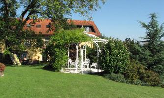 A beautiful garden with green meadows and a pavilion. In the background, a charming house can be seen.