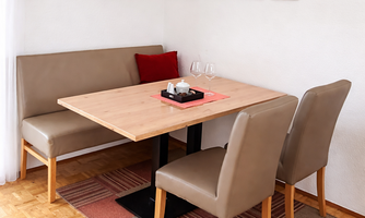 A cozy dining area with a wooden table and a bench. It includes two chairs, a decorative rug, and a modern lamp.