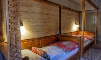 A cozy sleeping room with two wooden beds. The walls are made of rustic wood panels, and soft light creates an inviting atmosphere.