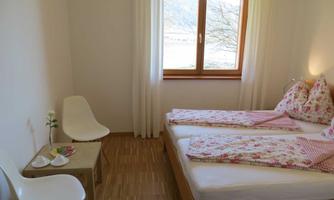 A cozy bedroom with two beds, blooming pillows, and a large window. A small table and a chair complement the furnishings.