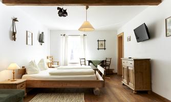 A bright room with two beds and cozy wooden furniture. There is a window with curtains and a television on the wall.