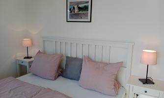 A cozy bedroom with a white bed and large, colorful pillows. Next to the bed are two nightstands with lamps.