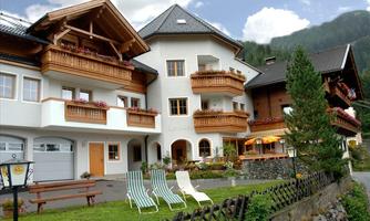 A charming alpine house with balconies and flowers. In the foreground, there are reclining chairs on a green meadow.