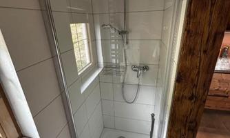 A modern shower with glass partition and bright tiled floor. The room has a window that provides natural light.