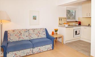 A cozy living room with a blue sofa and a modern kitchen. The room is bright and cheerful, with a lovely table decoration and plenty of space.