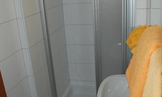 A small bathroom with a shower cabin and a sink. Orange towels are hanging on the wall.