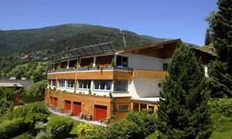 A modern building in a beautiful mountainous landscape. Surrounded by green trees and a clear blue sky.