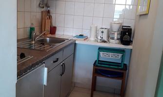 A small kitchen with a silver sink and kitchen unit. On the countertop, there are a coffee machine and appliances, and a wall shelf is hanging.