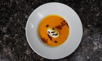 A creamy pumpkin cream soup in a white bowl. The soup is decorated with drops of vinegar and pumpkin seeds.