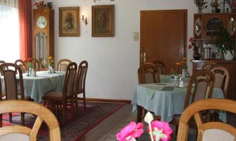 A cozy restaurant with wooden furniture and tablecloths in soft colors. Flowers in the center of the tables create an inviting atmosphere.