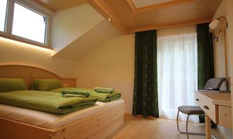 A cozy bedroom with a double bed and green bedding. The room has large windows and a wooden ceiling, creating a warm atmosphere.