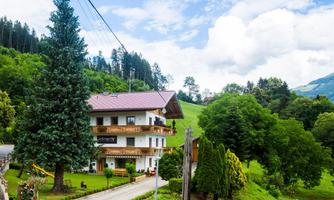 A cozy house nestled among green hills and trees. The sky is slightly overcast and the surroundings are calm and inviting.