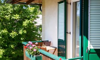 A quiet balcony with flower boxes and a small table. In the background, green trees can be seen.