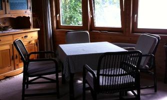 A cozy room with a table and several chairs. Large windows let in plenty of daylight.