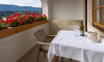 A beautiful balcony with a view of the mountains, blooming red geraniums, and a set table. The cozy atmosphere invites you to relax.