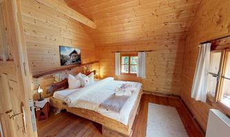 A cozy wooden room with a large bed and warm ambiance.  
Large windows let in plenty of light and offer a view outside.