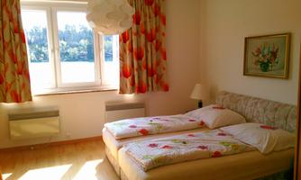 A cozy bedroom with two beds and colorful curtains. The view from the window shows a green landscape and plenty of daylight.