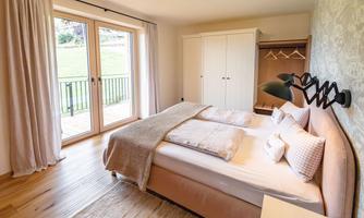 A modern bedroom with a comfortable double bed and a bright wood floor. Large windows let in plenty of natural light and provide access to a balcony.