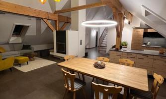A modern living room with a large wooden table and chairs. Bright ceiling lights and a cozy seating area create an inviting atmosphere.