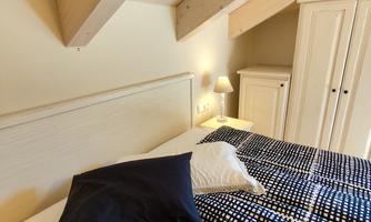 A cozy bedroom with a large bed and modern furniture. The ceiling has visible wooden beams and warm lighting.