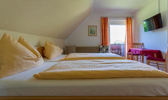 A cozy bedroom with two beds and yellow pillows. The room has a window with a view and a small table next to a chair.