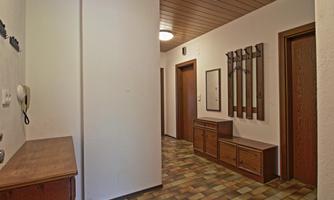 A bright hallway with gray flooring and wooden furniture. Hooks for coats and a mirror hang on the wall.
