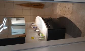 A modern bathroom with a wavy sink and mirrors. The walls are tiled, and there is a towel holder as well as some toiletries on the shelf.