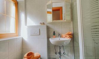 A modern bathroom with a shower and toilet.  
Orange towels are placed on the toilet and a window provides daylight.