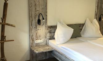 A cozy bedroom with a wooden bed and modern pillows. The walls are painted in neutral colors and there is a natural wood decoration.