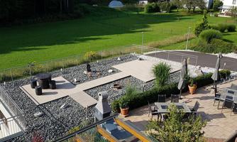 A modern terrace with stone flooring and several seating areas. In the background, a green meadow can be seen.