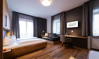 A modern hotel room with two beds and a cozy seating area. Large windows provide plenty of daylight and a pleasant atmosphere.