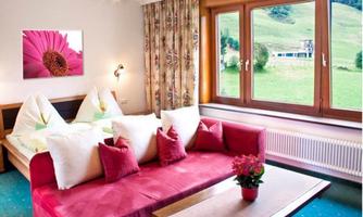 A cozy hotel room with a red sofa and colorful cushions. Large windows provide a view of the green landscape.