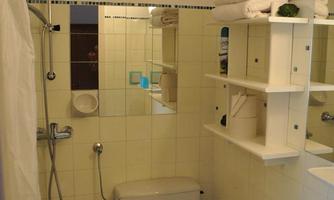 A small bathroom with a shower, toilet, and sink. Shelves with towels and decorations are mounted on the wall.