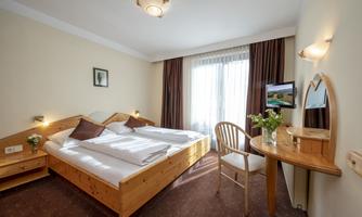 A cozy room with a double bed and wooden furniture. Large windows provide plenty of daylight and a welcoming atmosphere.