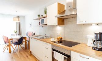 Modern kitchen with wood countertop and white cabinets. An adjacent dining area with a table and chairs is also visible.