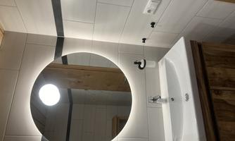 A modern bathroom with a round mirror and soft lighting. The wash area features a clear, white sink surface and wooden accents.