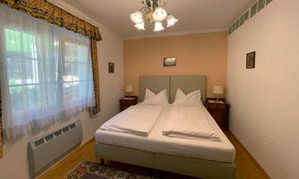 A cozy bedroom with a large bed and two nightstands. The room has a window with curtains and a rug on the floor.