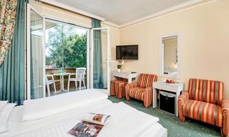 A cozy hotel room with two beds and a television. The balcony offers a view of nature, and there is modern furniture.