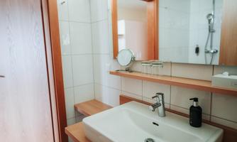 A modern bathroom with a white sink and a mirror. The walls are brightly tiled and there are wooden shelves.