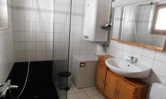A modern bathroom with a shower and a sink. The walls are tiled with white tiles and there are wooden cabinets for storage.
