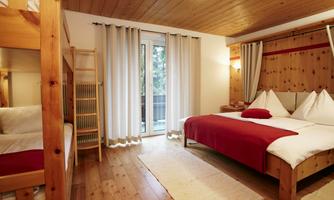 A cozy room with a double bed and a bunk bed. Large windows provide plenty of daylight and a view outside.