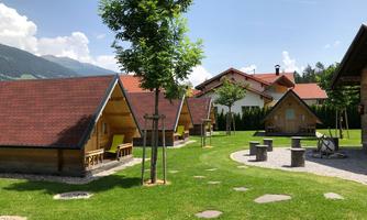 A charming landscape with wooden huts and green grass. In the background, gentle hills and a clear sky are visible.