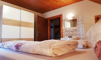 A cozy bedroom with a large bed and a wardrobe. There is a mirror on the wall and the ceiling is made of wood.