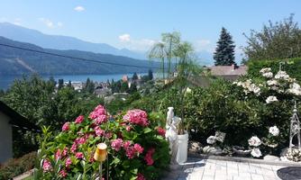 A beautiful view of a lake, surrounded by mountains. Colorful flowers in the foreground and a clear blue sky make the scene inviting.