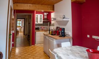 A modern kitchen with a red accent wall and wooden ceiling. The dining area is simple and inviting with a table and chairs.