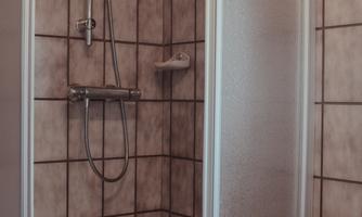 A modern shower cabin with tiles and a handheld shower. Next to the shower, orange towels are stacked.
