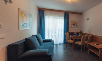 A cozy living room with a blue sofa and a dining area. Large windows let in plenty of light.