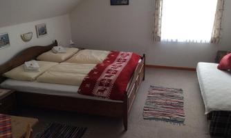 A cozy bedroom with a double bed and a single bed. The room has a window with curtains and a carpet on the floor.